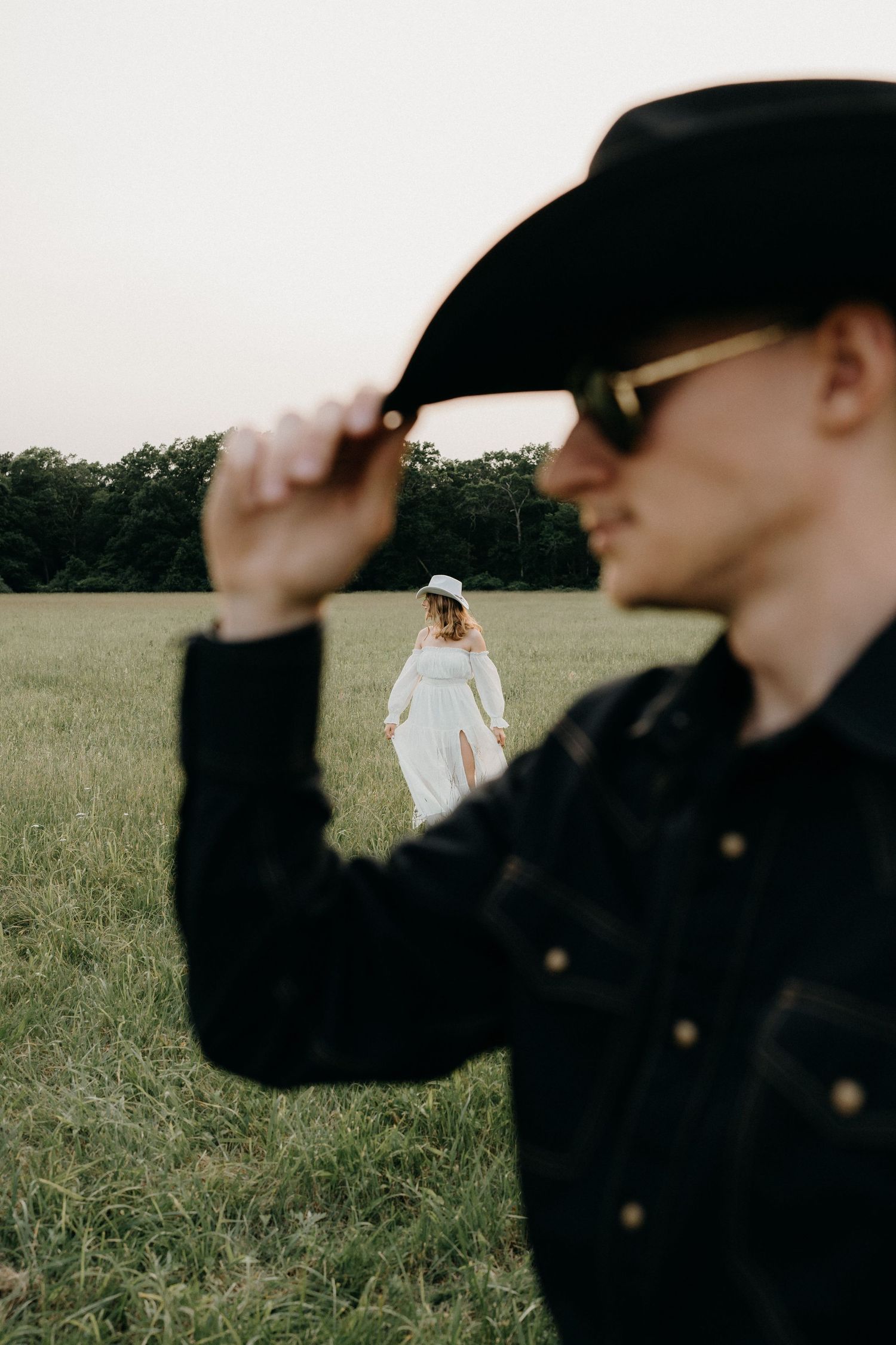 A person in black stands in foreground while white-dressed figure appears in distant field.