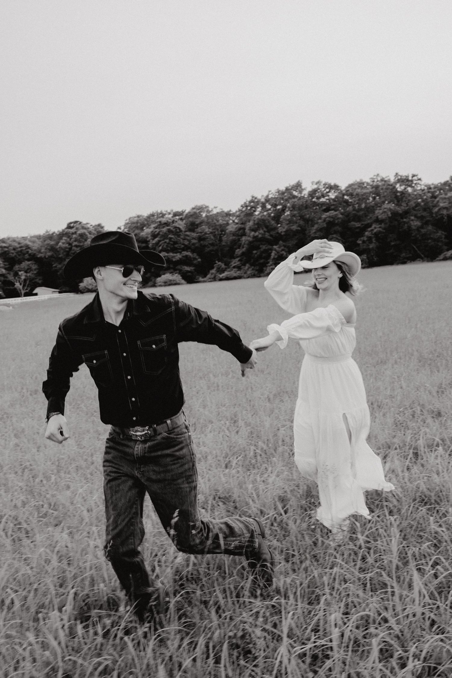 A playful black and white photo of a couple dancing in a meadow.