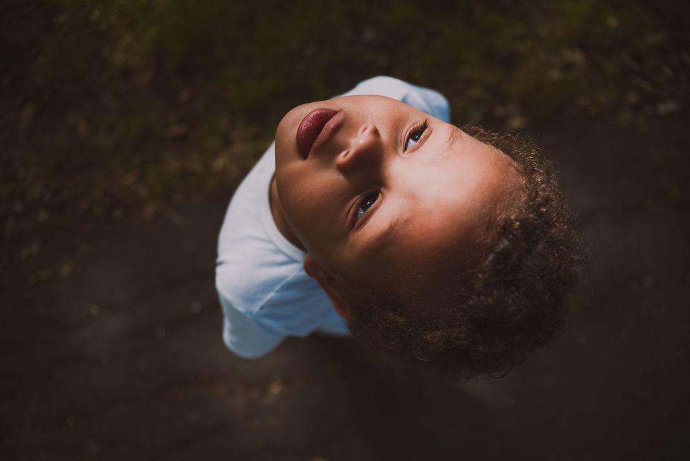 A child gazing upward against dark background with dramatic lighting effect.