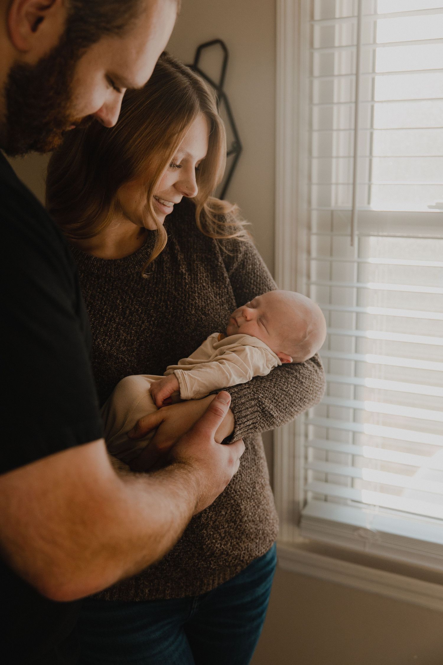 A tender moment between parent and newborn in warm, natural light by a window.