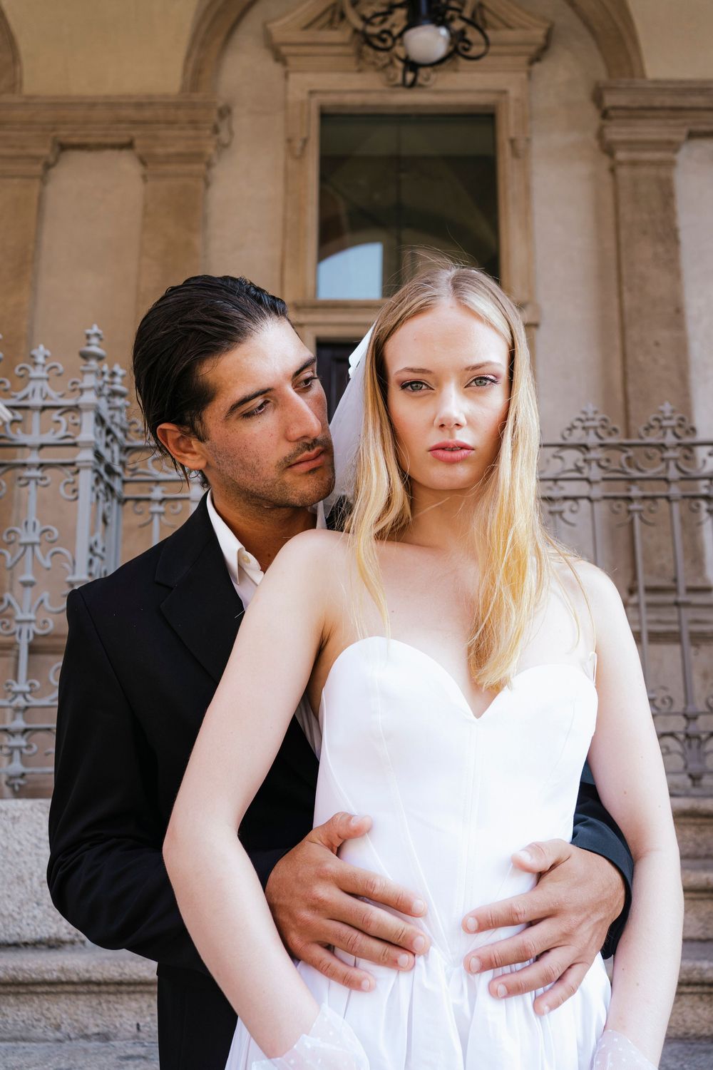 A romantic couple poses together against stone columns in an elegant architectural setting.