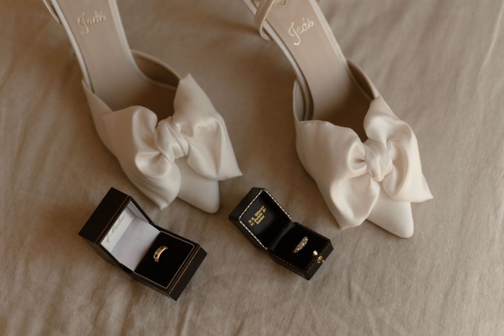 Wedding rings and white satin bow arranged artistically on beige surface.