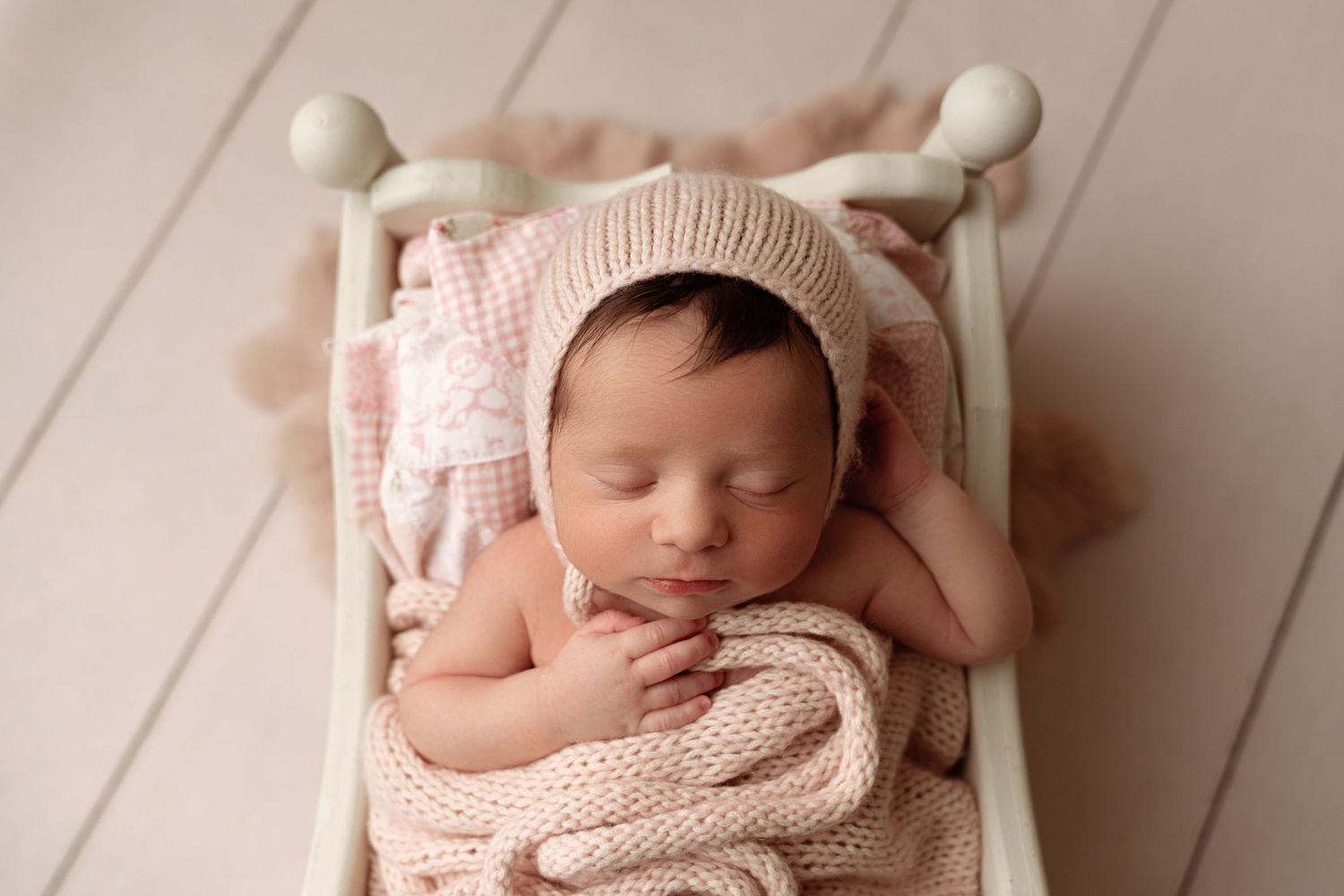 A sleeping newborn wrapped in cozy beige knit blanket rests peacefully in a wooden bowl against rustic background.