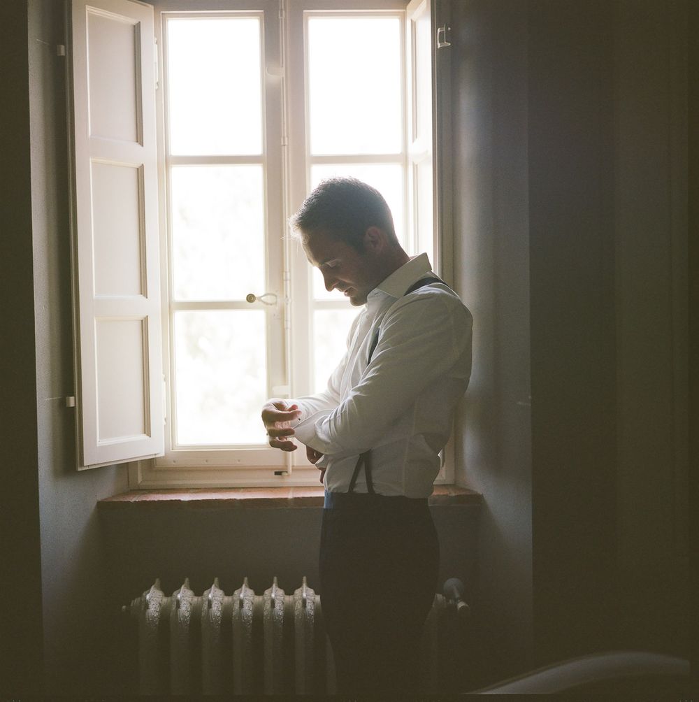 Silhouette by a bright window adjusting cufflinks in preparation for a formal event.