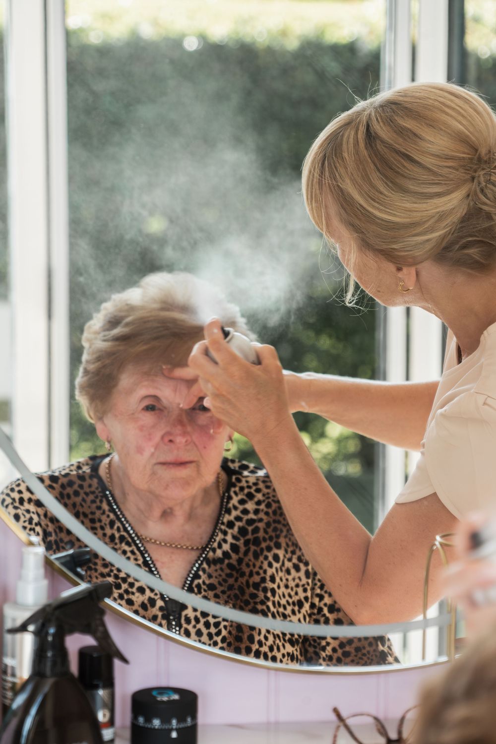 A caregiver helps an elderly woman with oxygen therapy near a window in natural lighting with smoke visible.