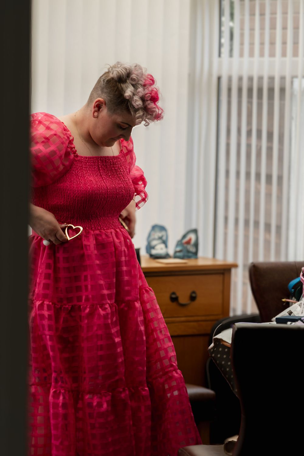 A child in a flowing red formal dress with puff sleeves and floral hair accessories stands in a living room.