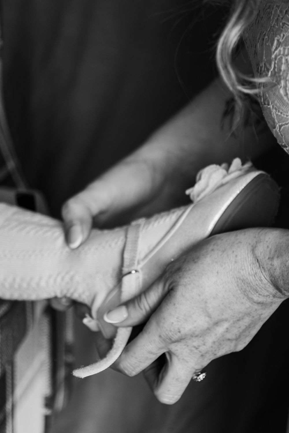 Black and white close-up of hands fastening or adjusting a white garment showing fine detail.