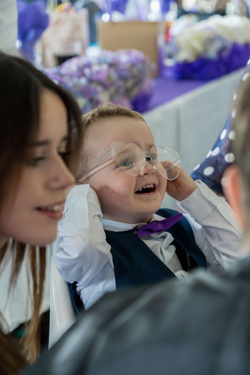 Young attendee in glasses, white shirt and purple bowtie laughs joyfully at formal event.