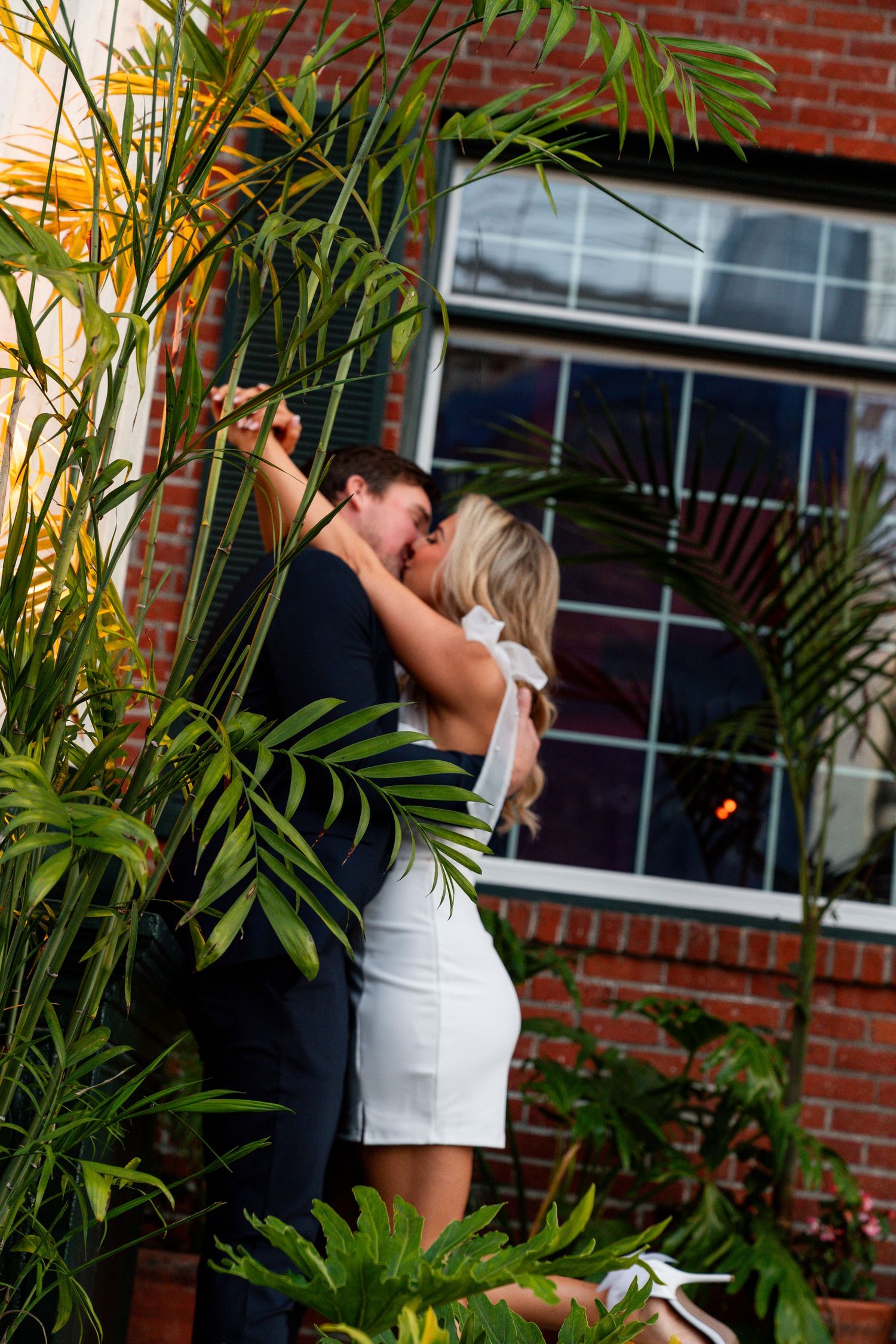 Jessica Paige Photo Co. Best San Diego Wedding Photos. Romantic moment between couple among tropical plants against brick building backdrop.