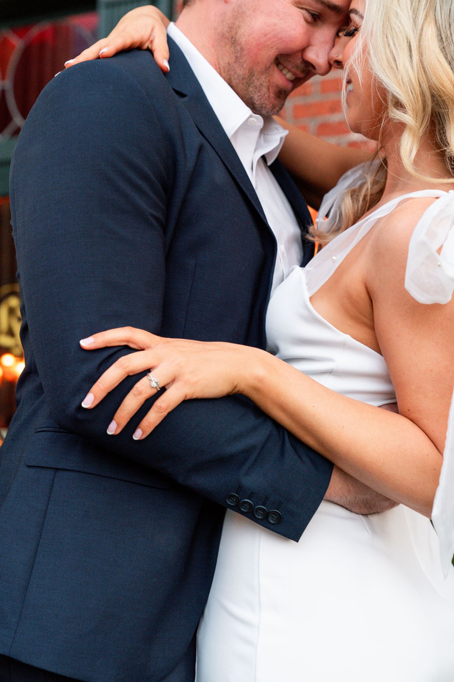 Jessica Paige Photo Co. Best San Diego Wedding Photos. Close up of couple embracing, showing details of formal attire against brick wall.