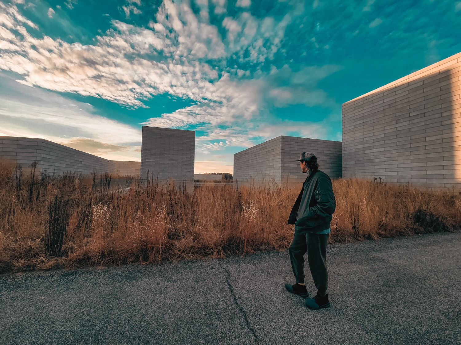 Person standing near concrete walls under dramatic turquoise sky with wispy clouds.
