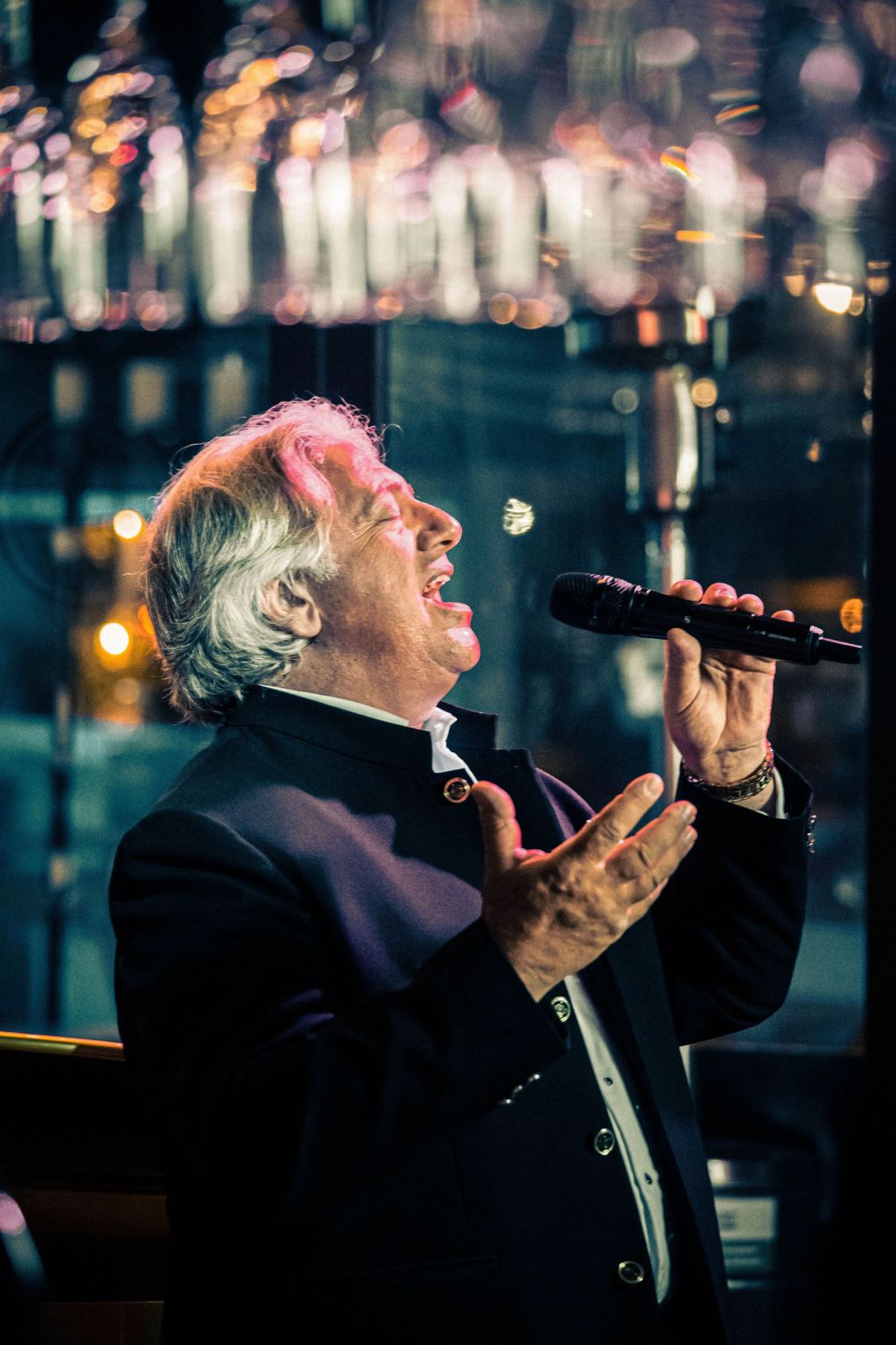 A performer in black attire sings passionately into a microphone with bokeh lights glimmering in the dark background. Photography Gold Coas