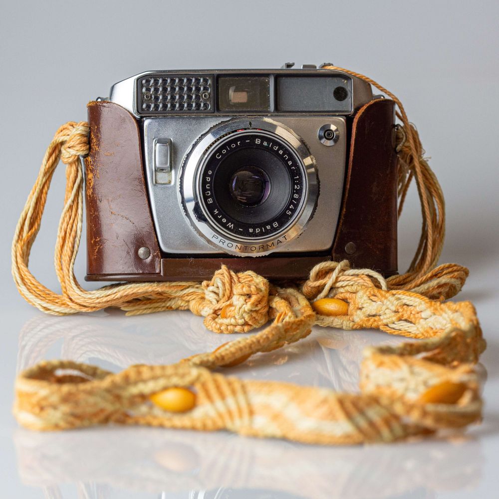 Vintage camera with leather case rests beside a decorative yellow fabric cord on a light surface. Photography Gold Coast