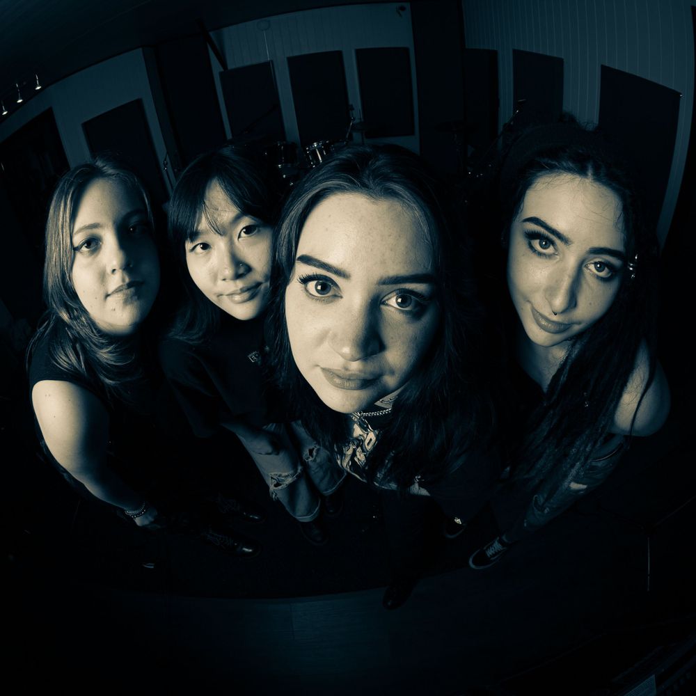 A fisheye lens captures a dramatic close-up portrait of four women with dark hair against a dark background. Photography Gold Coast