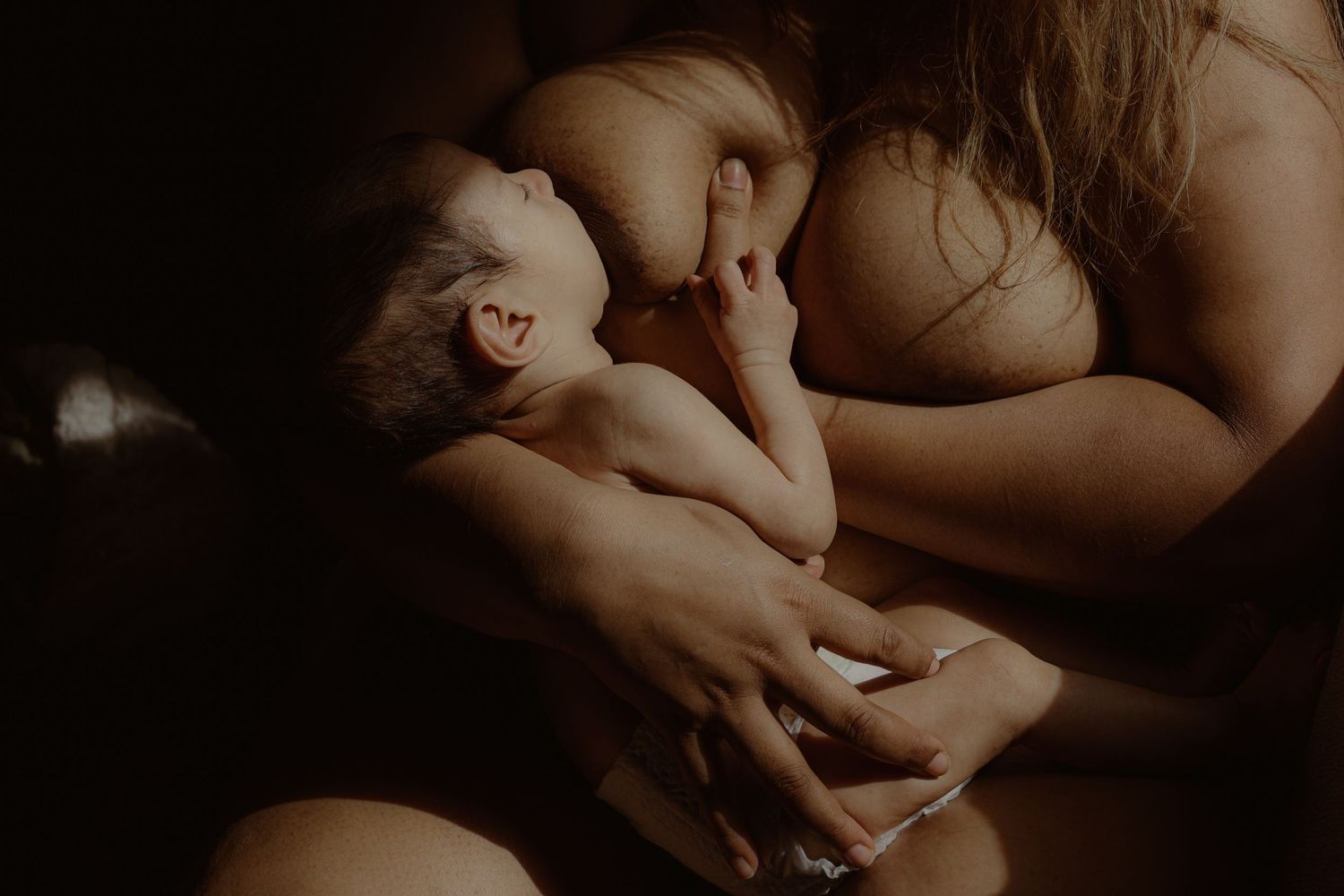 close up in colour of woman breast-feeding newborn, intimate motherhood in Suffolk,natural light