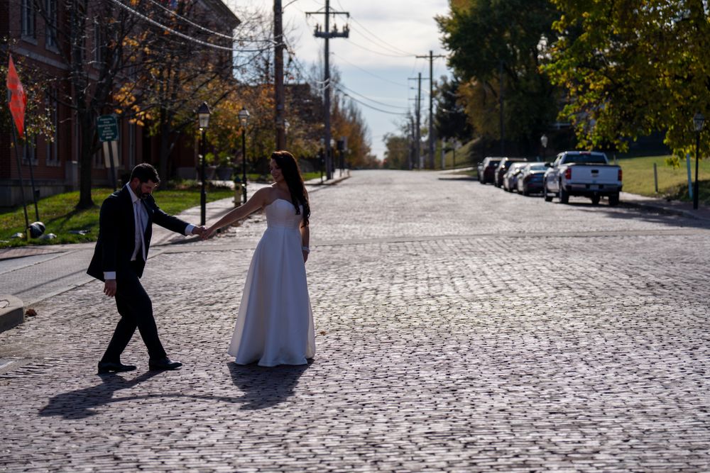 A couple in wedding attire walks down a cobblestone street on their special day.