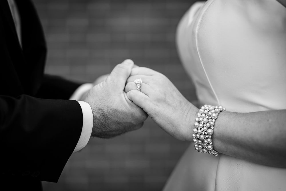 Close-up of clasped hands showing wedding rings and elegant bridal jewelry.