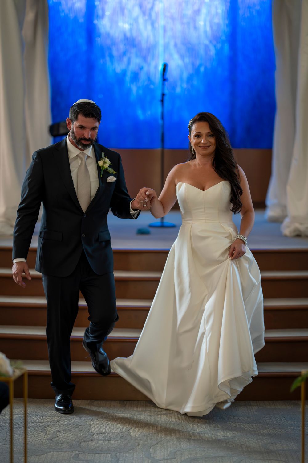 Newlyweds walking down church steps with a vibrant blue backdrop during their wedding ceremony.