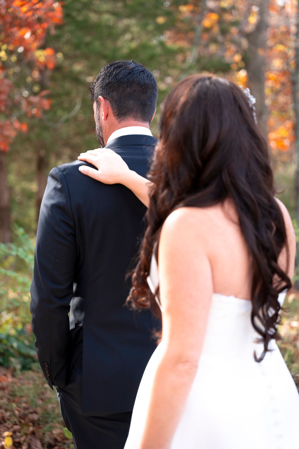 Autumn outdoor wedding photo showing couple from behind amidst fall foliage.
