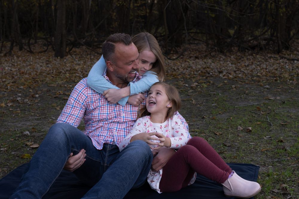 A family shares laughter while sitting together outdoors during a photo session.