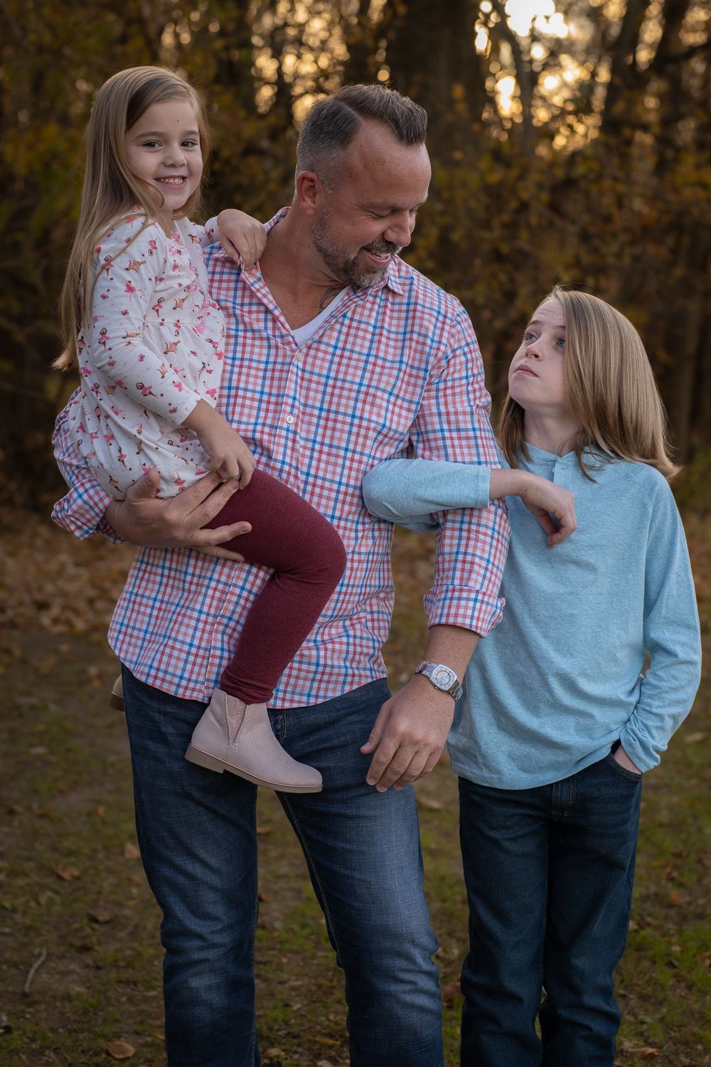 Family portrait outdoors with children and adult in casual clothing at sunset.
