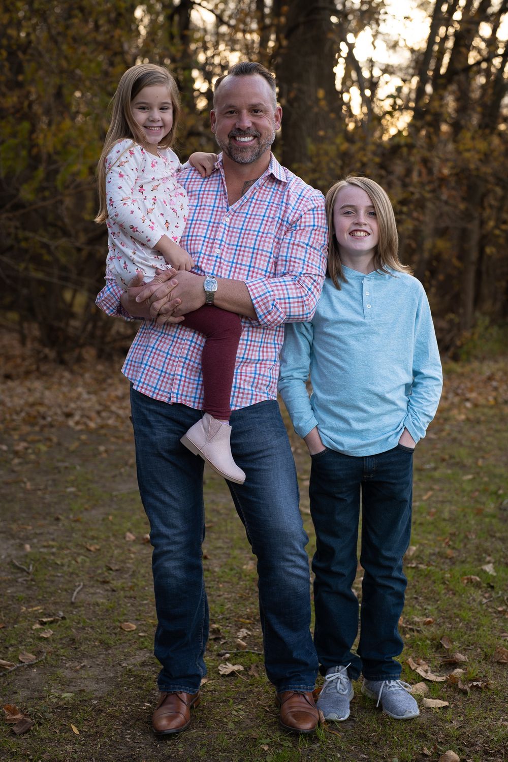 Happy family group poses together outside during golden hour in forest setting.