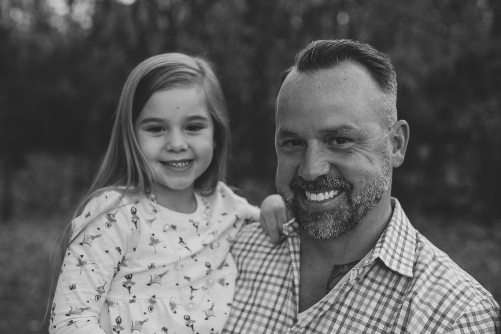 Black and white portrait of smiling parent and child outdoors.