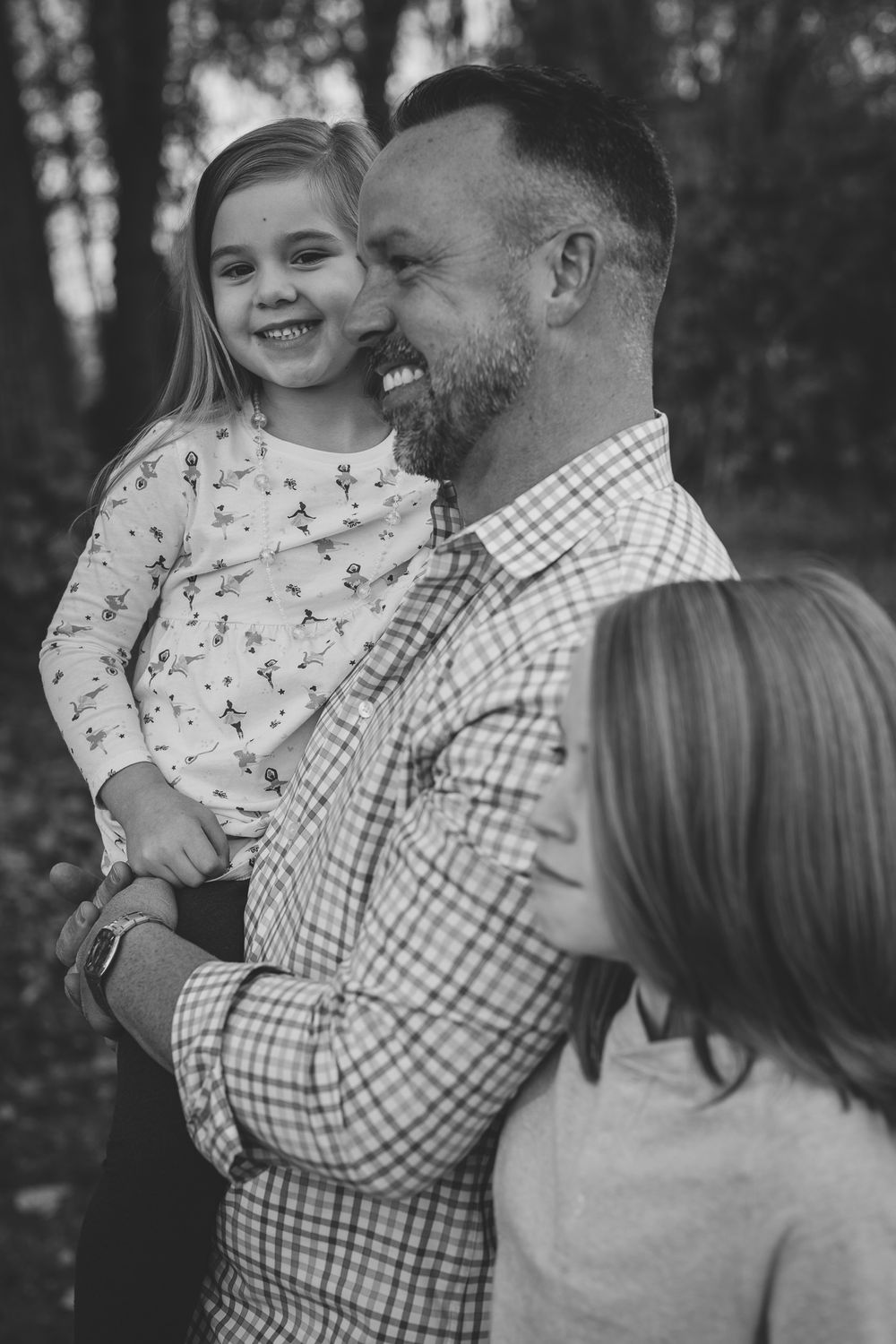 Black and white candid family moment captured outdoors with joyful expressions.