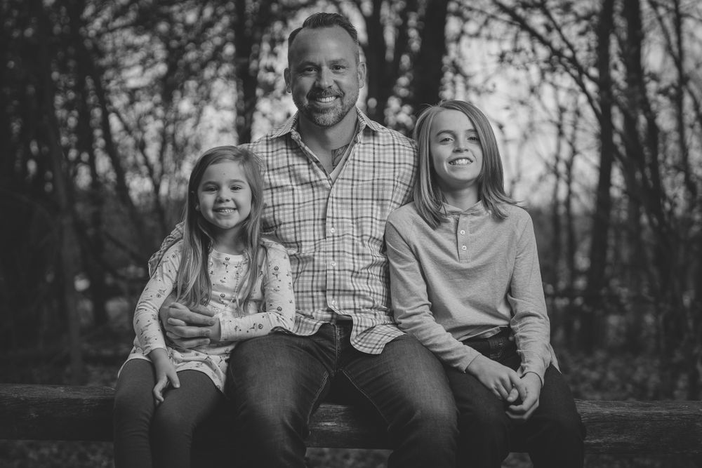 Black and white family portrait on wooden bench in natural setting.