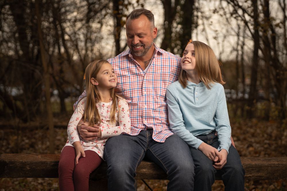 Family sitting together on wooden bench during autumn sunset photo session.