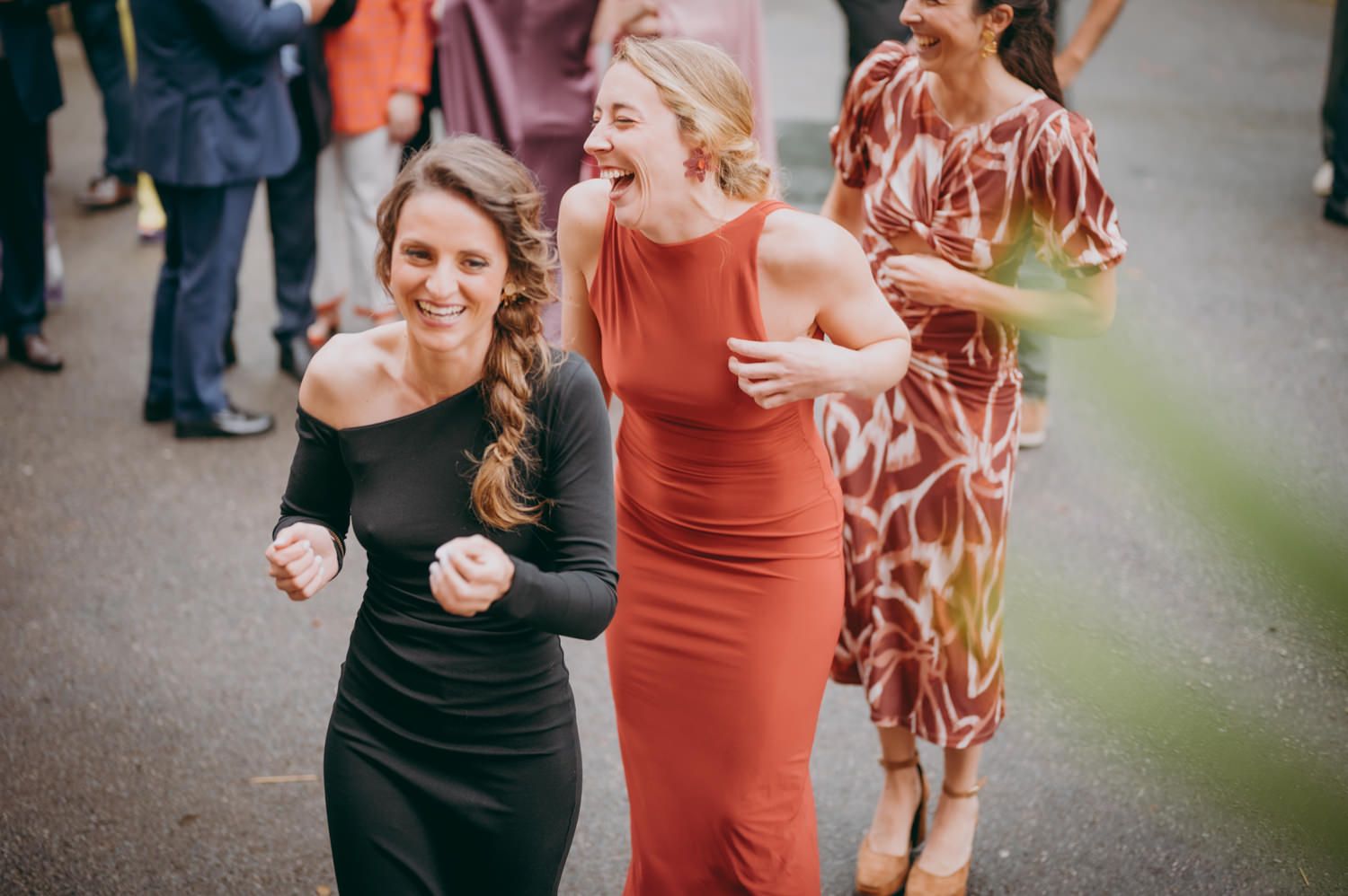 Invitados a la boda con elegantes vestidos riendo y bailando juntos en una celebración al aire libre.