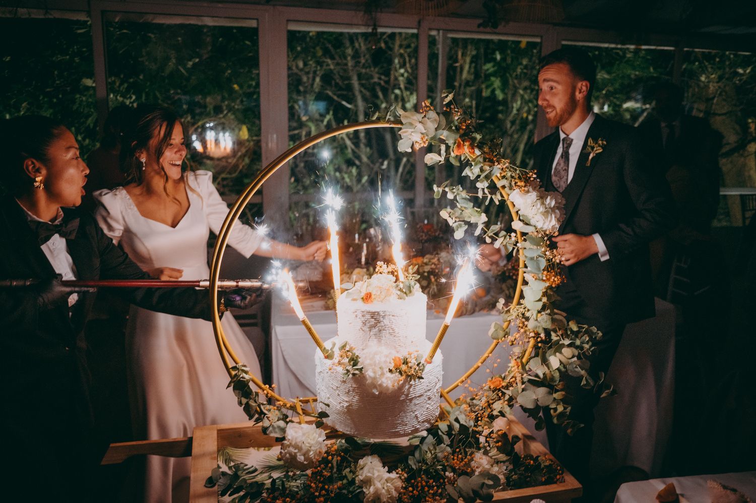 Celebración de boda con aros florales iluminados y bengalas que crean un ambiente mágico por la noche.