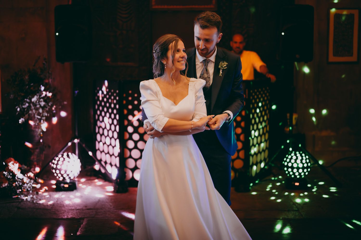Un momento de baile romántico iluminado por luces decorativas y patrones geométricos en una celebración nocturna del Palacio de Villabona.