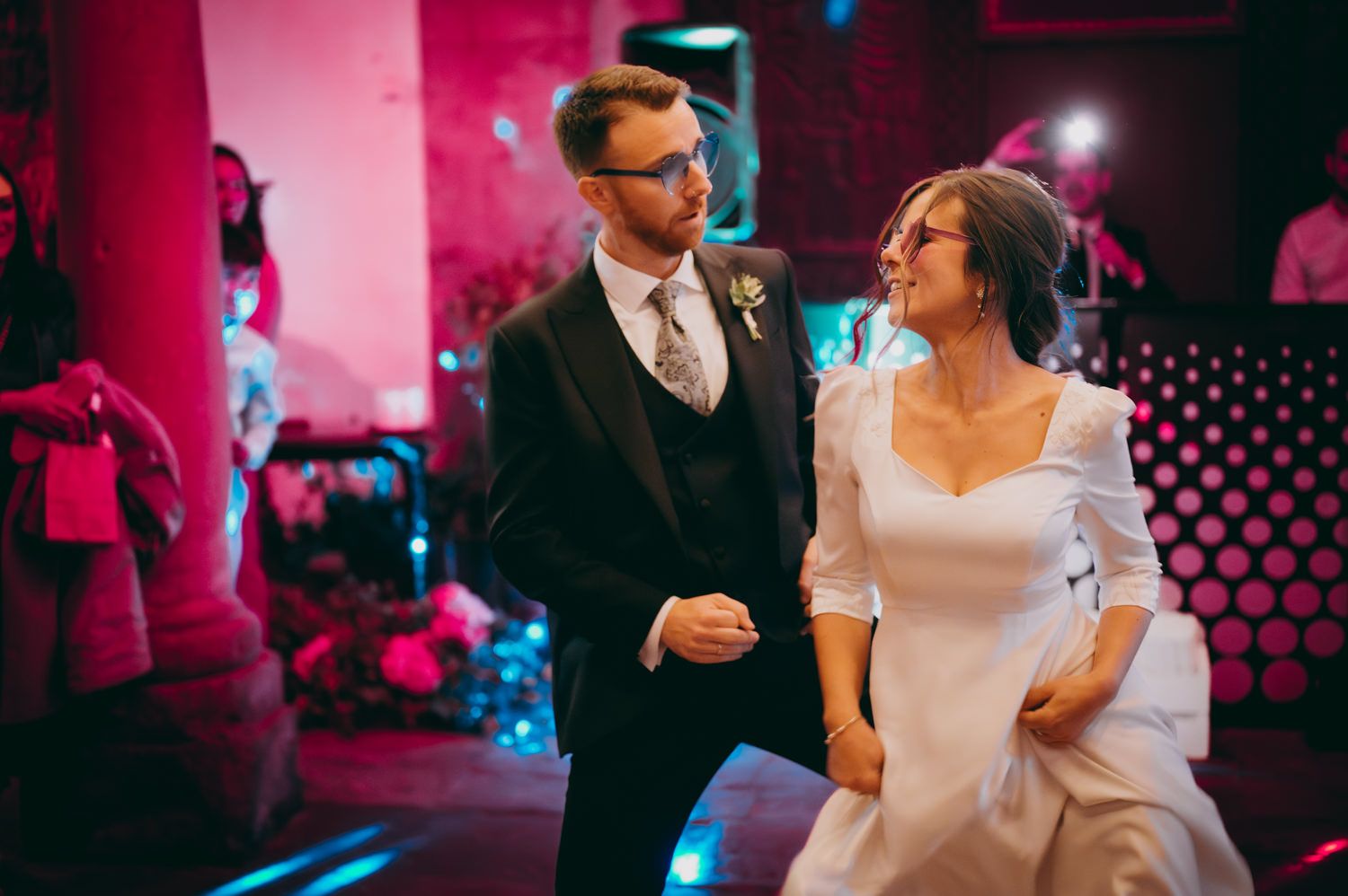 Unos novios baila en lafiesta de su boda en un lugar poco iluminado con iluminación rosa y elementos decorativos en el palacio de Villabona