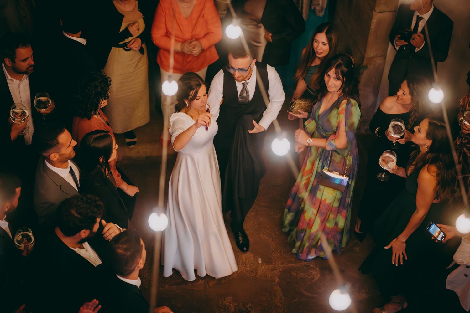 Novios bailan en una boda con una iluminación dramática e invitados rodeándoles en el Palacio de Villabona.