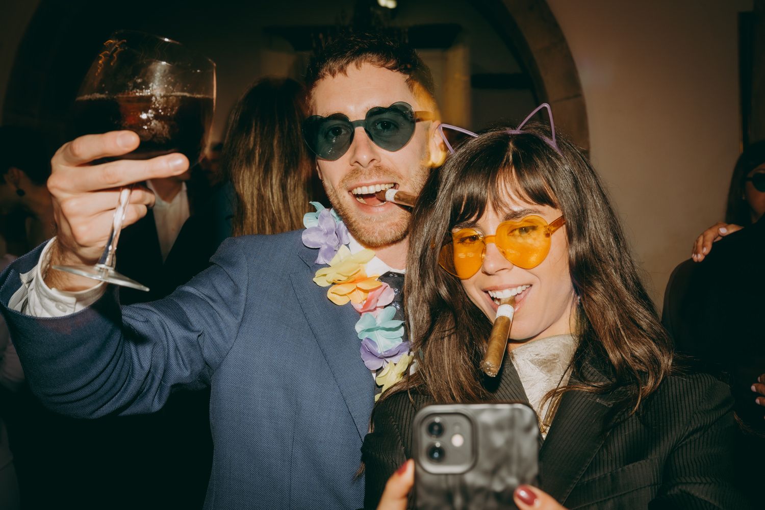 Los invitados a la boda, que llevan gafas de sol de colores, posan con bebidas en una celebración en el interior del Palacio de Villabona