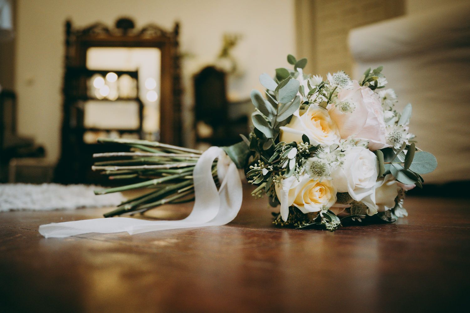 A beautiful wedding bouquet with white and pink roses and eucalyptus lying on a wooden table.
