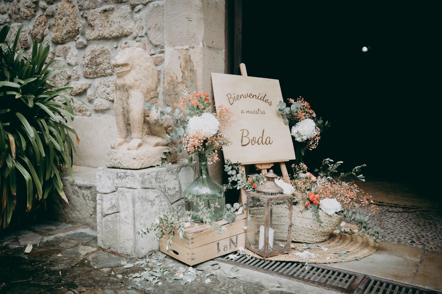 Decoración de boda vintage con un cartel de madera rústica, flores y elementos decorativos contra una pared de piedra