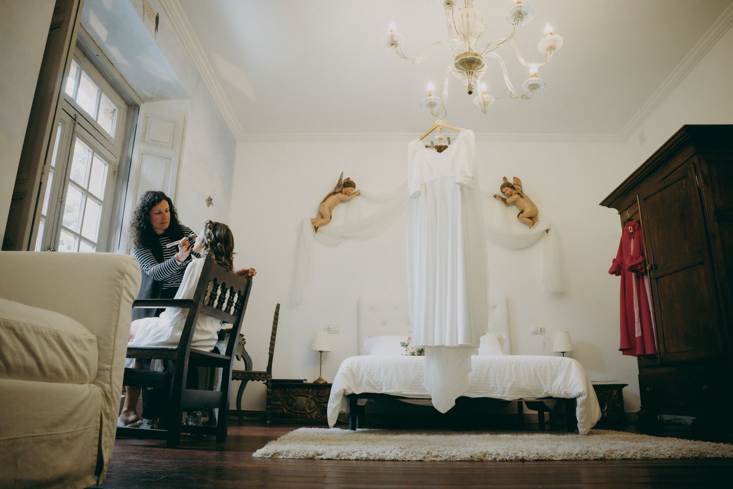 Una acogedora habitación blanca cuenta con un sofá, sillas vintage, lámpara de araña y astas doradas decorativas montadas en las paredes.