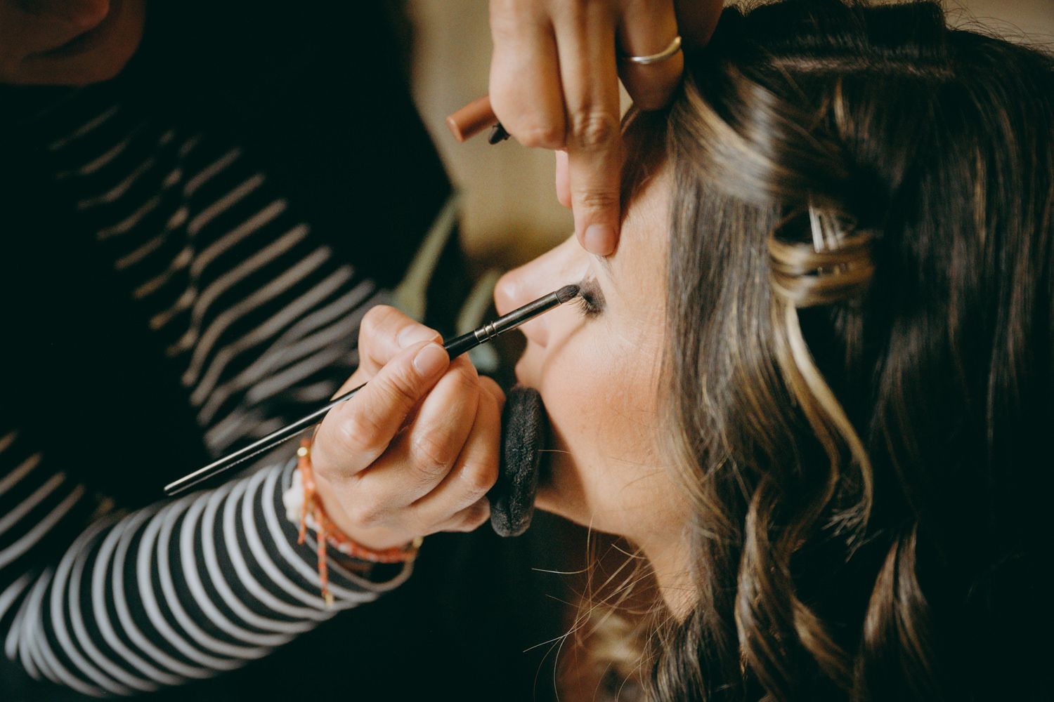 La maquilladora en camisa a rayas aplica lápiz labial durante la preparación nupcial.