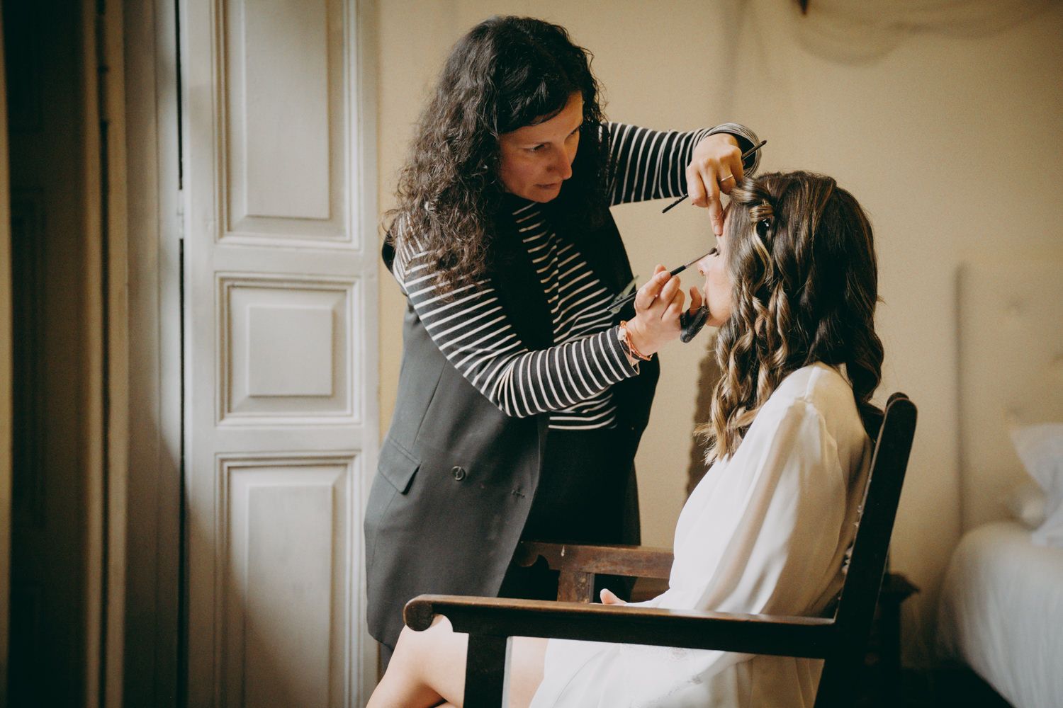 Estilista del cabello con top a rayas peina el cabello durante la preparación de la boda.