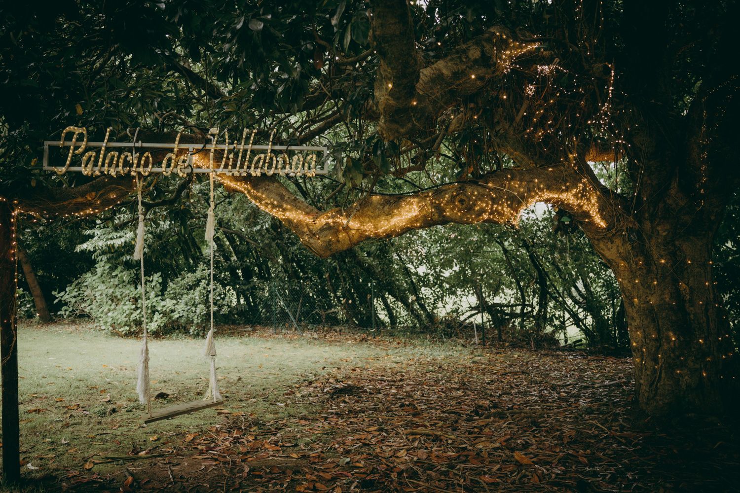 Un cartel rústico de bienvenida de madera cuelga en un entorno de bosque con hojas otoñales cubriendo el suelo del Palacio de Villabona.