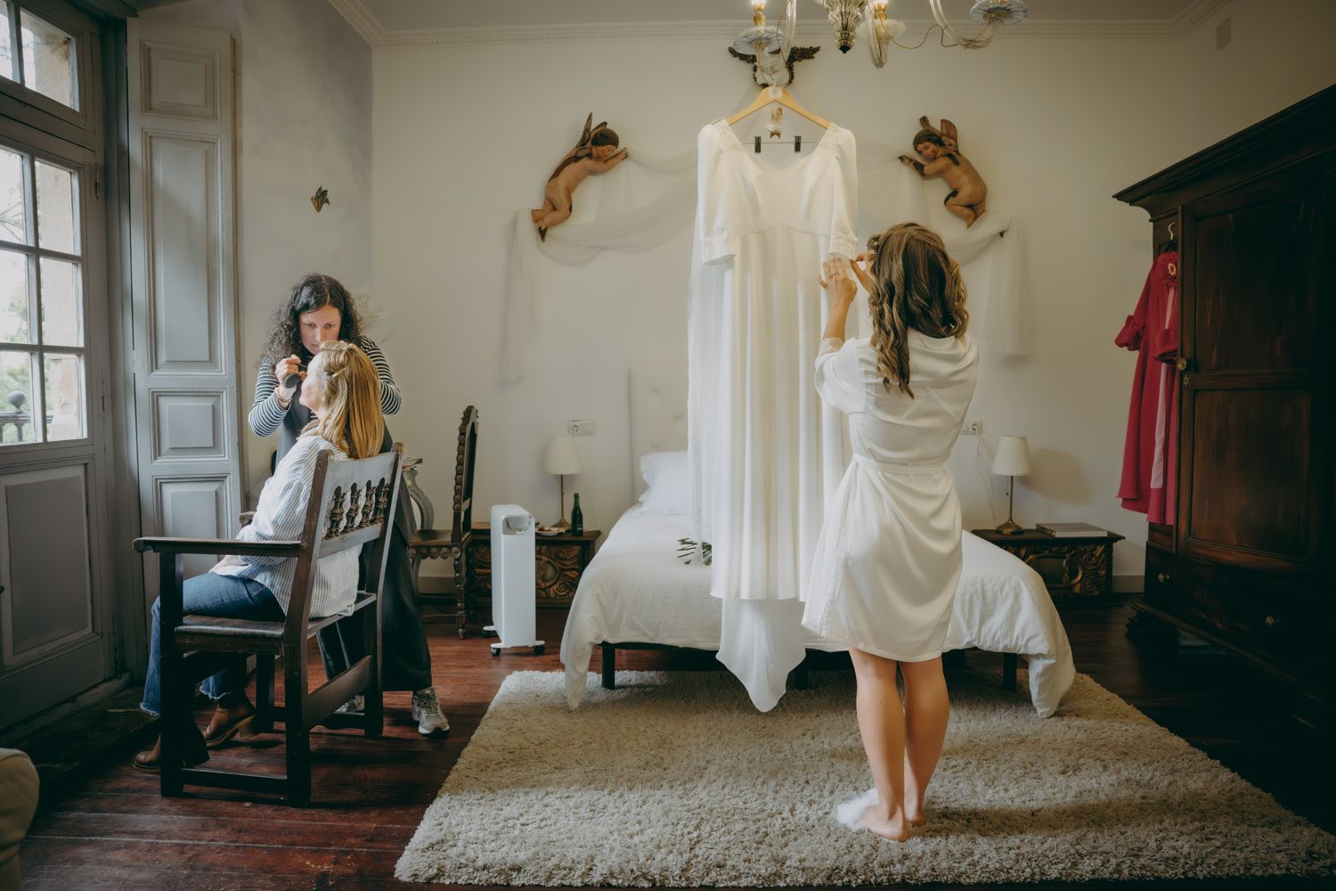 Un vestido de novia cuelga en una habitación mientras alguien con una bata se prepara para el día.