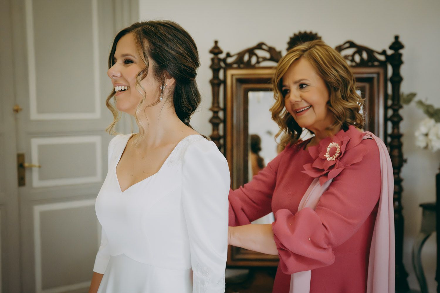 Escena de preparación con un vestido blanco y un traje rosa frente a un espejo adornado.