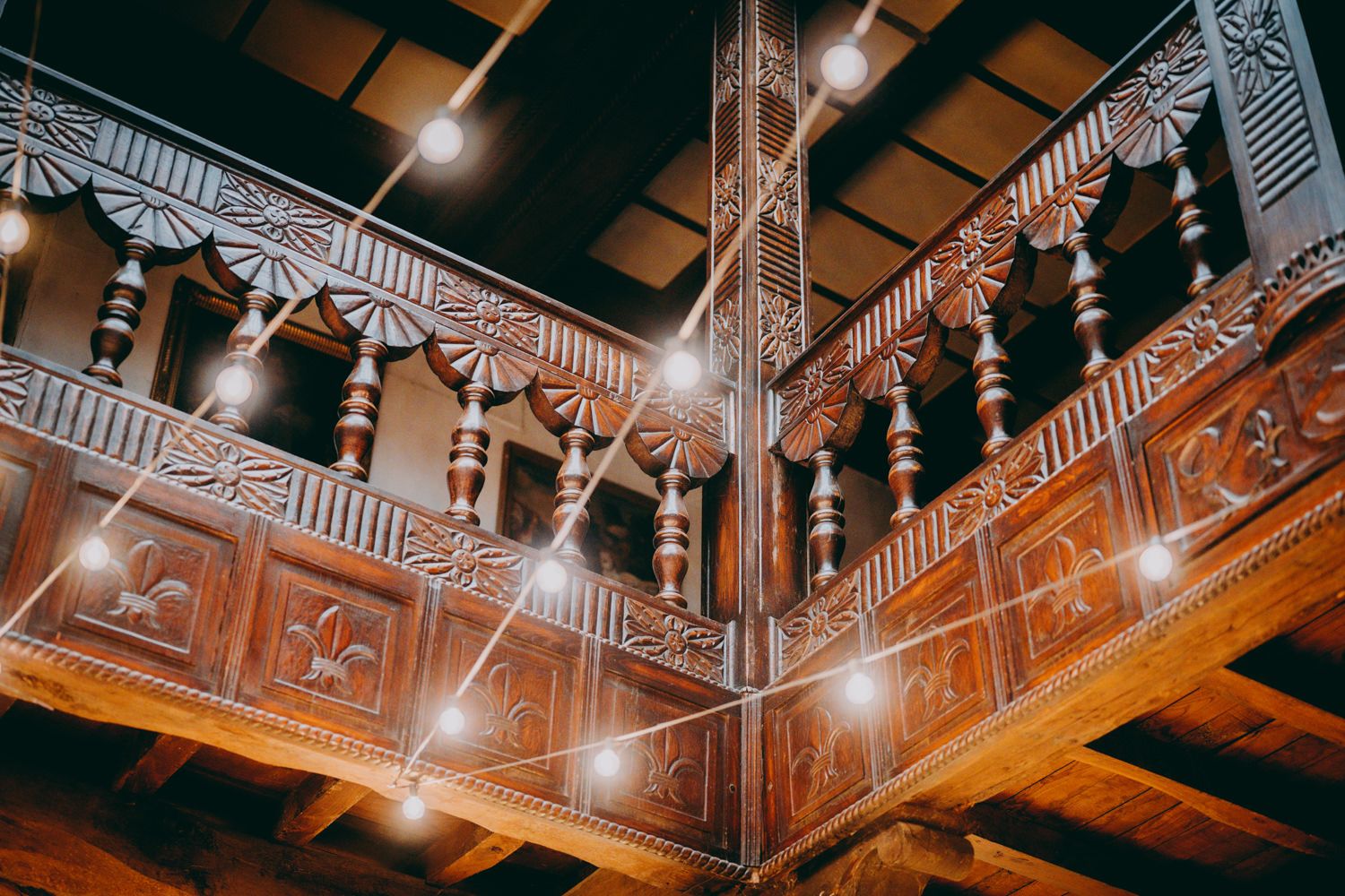 Balcón de madera tallada adornado con detalles intrincados y elementos arquitectónicos en una iluminación cálida.