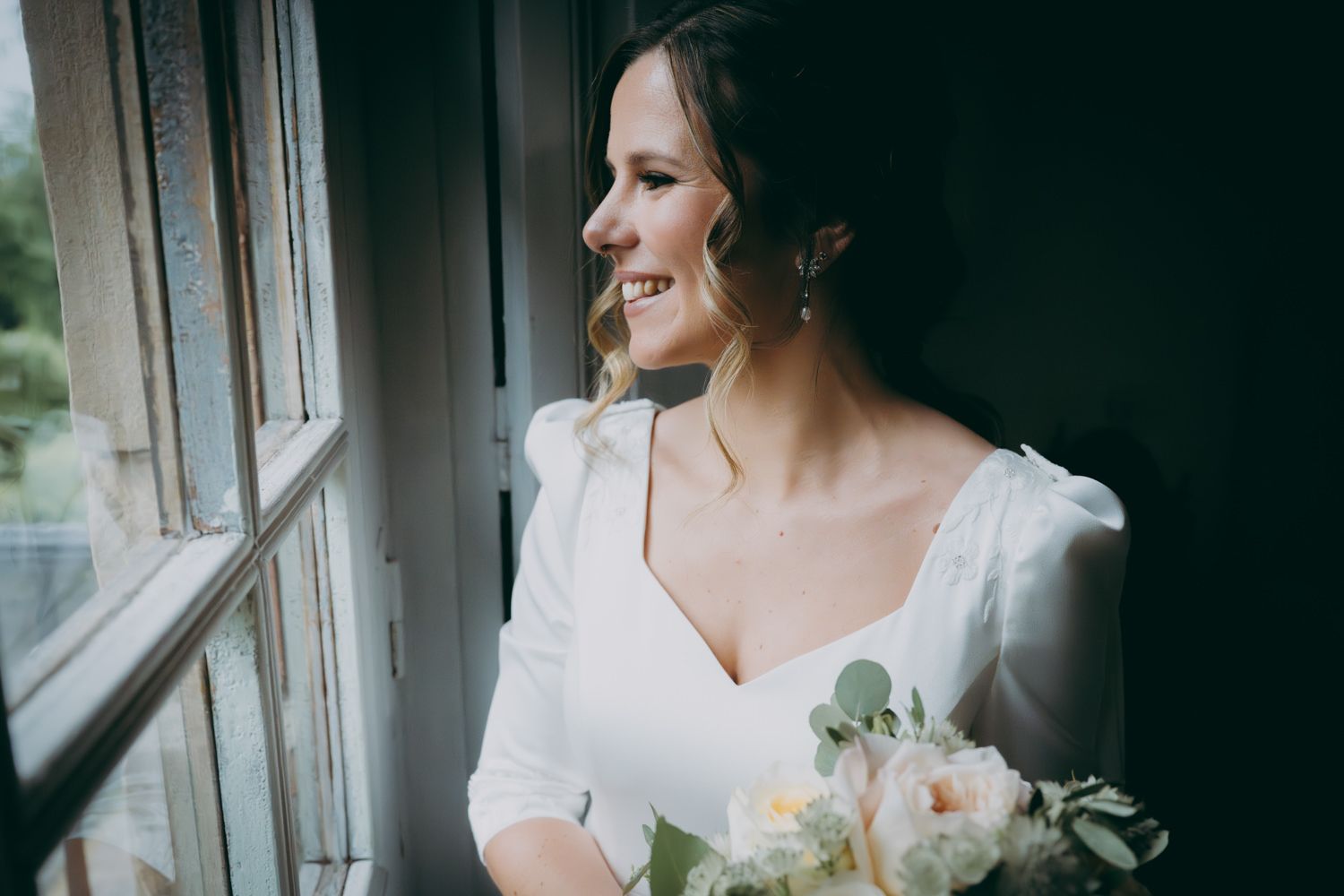 Momento nupcial espontáneo junto a la ventana con un suave ramo de flores