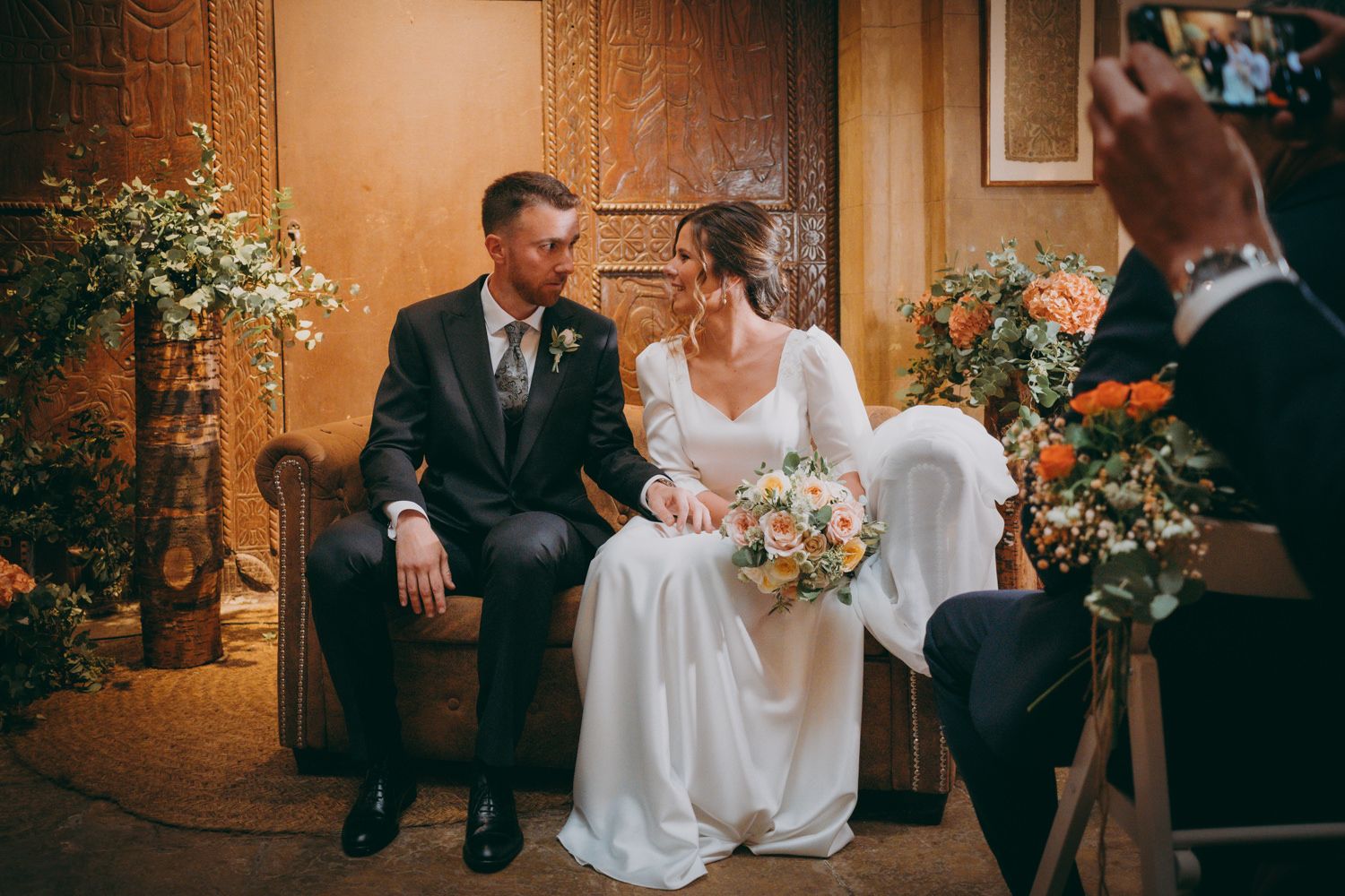 Pareja sentada en una silla vintage rodeada de delicados arreglos florales.