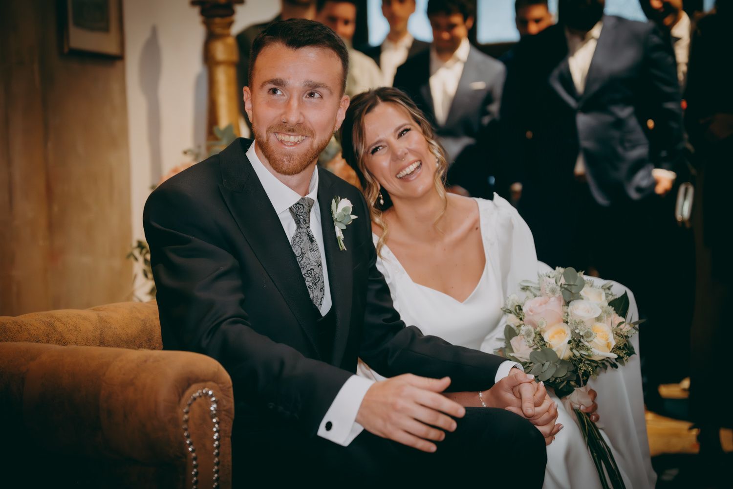 Una feliz pareja de novios se sienta junta en un sofá de cuero marrón durante su ceremonia.