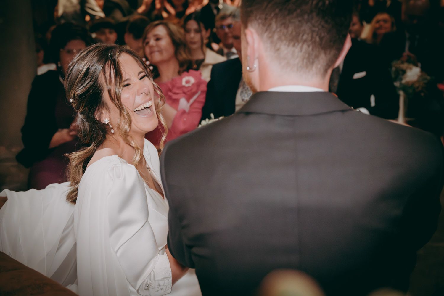 Una novia vestida de blanco riendo durante la recepción de una boda mientras baila con los invitados.