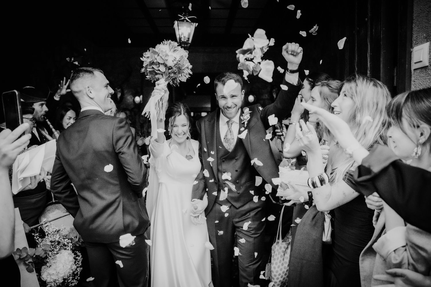 Una pareja de novios camina bajo una lluvia de confeti mientras los invitados vitorean durante una celebración de salida de la boda